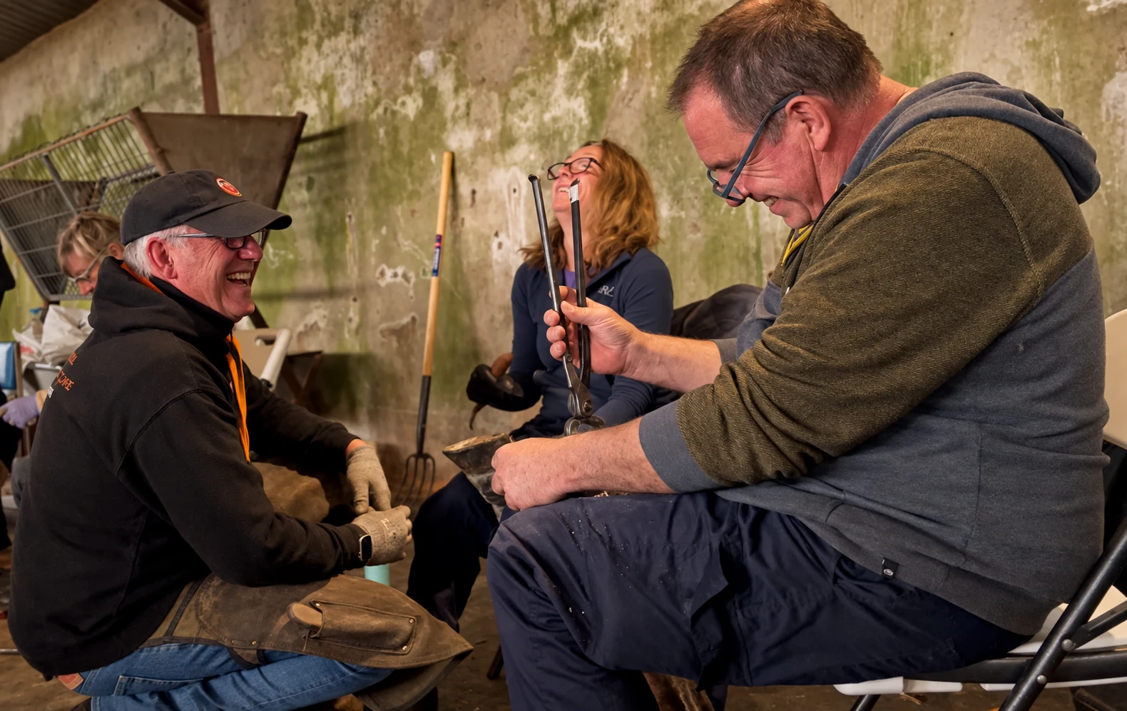 Three workshop participants laughing together during practical hoof work