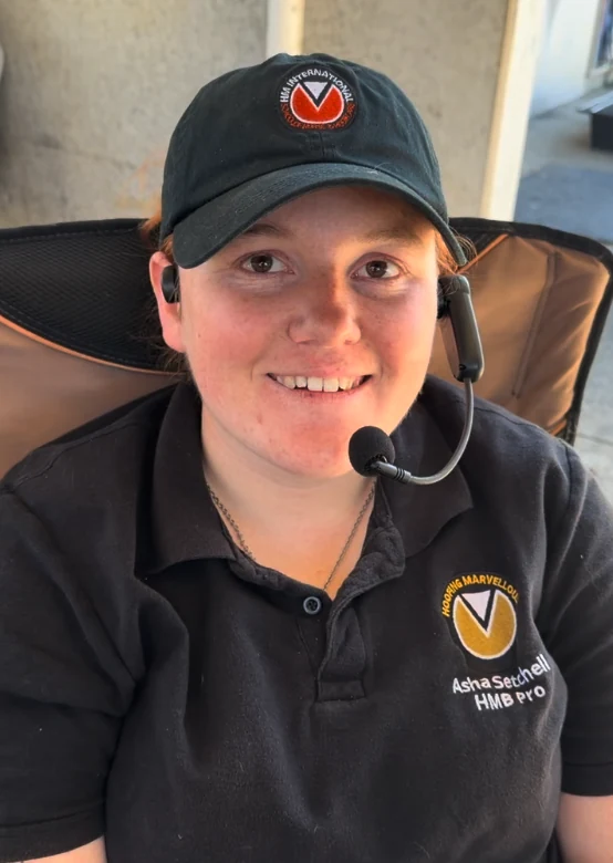 Asha Setchell, smiling, wearing an HM International cap and a Hoofing Marvellous polo shirt